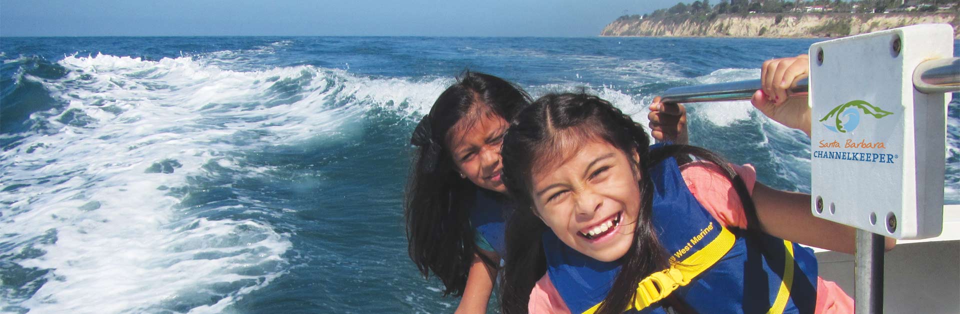 Happy kids smiling while their hands touch the water as they ride on a boat in the ocean.